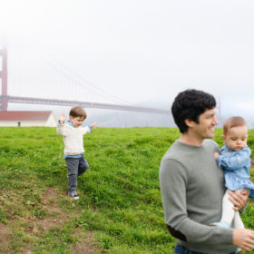 Little brother skipping along the grass as dad and little sister walks in front of Golden Gate Bridge in Crissy Field
