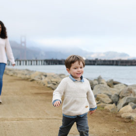 Little brother walking in front of mom and dad along the beach at Crissy Field with Golden Gate Bridge in background