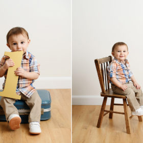 Baby boy sitting on vintage luggage and chair while holding number 1