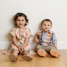 Big sister and little brother smiling for the camera on wood floor in studio