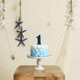 Blue mini cake with number 1 cake topper and starfish and net nautical background