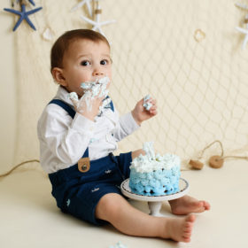 Baby boy stuffing face with blue frosting from nautical cake smash
