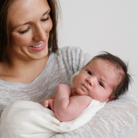 Mom wearing a gray sweater holding newborn baby girl and smiling in Sacramento studio