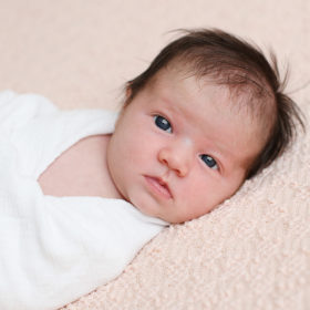 Newborn baby girl with blue eyes lying on a pink blanket and white swaddle in Sacramento studio