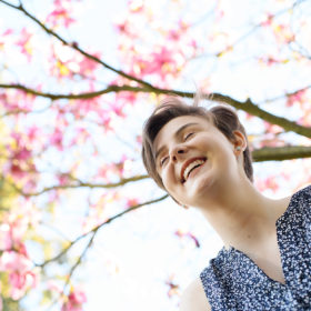 Teen girl smiling while camera looks up at pink flowers in trees outside of State Capitol