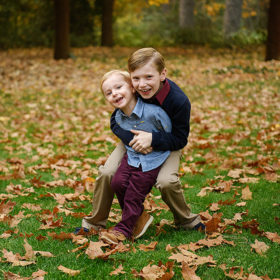 Brothers hugging each other on grass covered in autumn leaves in Grass Valley