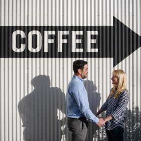 Couple holding hands in front of coffee sign in Sacramento