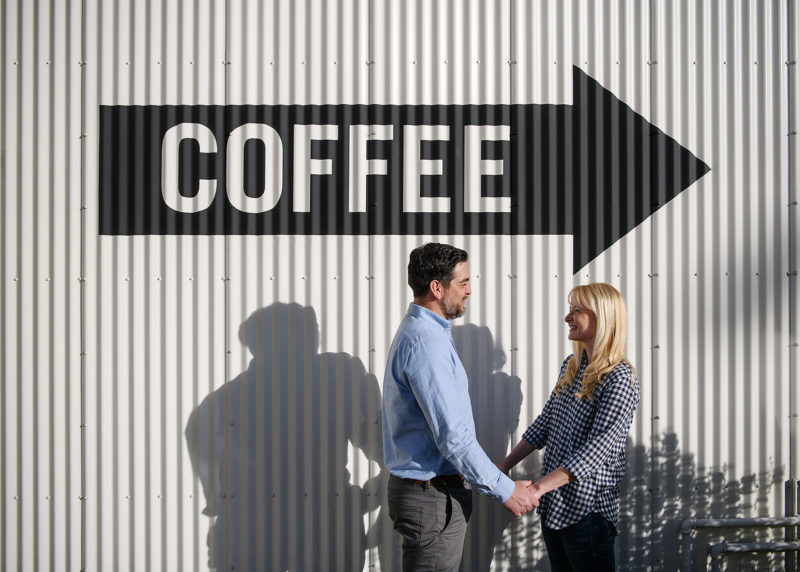 Couple holding hands in front of coffee sign in Sacramento