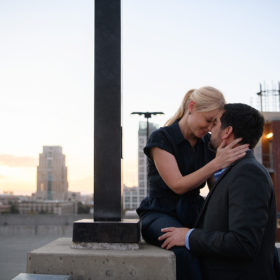 Couple staring at each other lovingly on top of Sacramento roof with city skyline in background