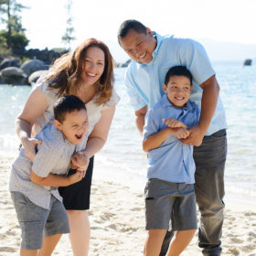 Laughing family on sandy Lake Tahoe shore with lake in the background