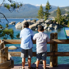 Brothers standing on walking bridge and looking at the view of the blue water in Lake Tahoe