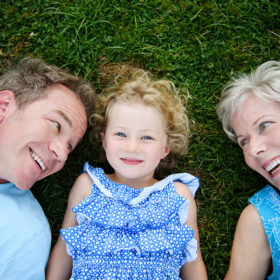 Three generations: dad, daughter and grandma lying on the grass and smiling at camera