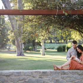Mom and dad look lovingly at newborn baby while sitting on park stone gazebo in Sacramento