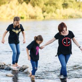 Mom and daughters wearing superhero shirts wading through river in Fair Oaks
