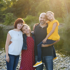Family photo in natural light with trees and river rocks as background in Fair Oaks