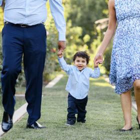 Baby boy walking in between mom and dad through McKinley Park Rose Garden Sacramento