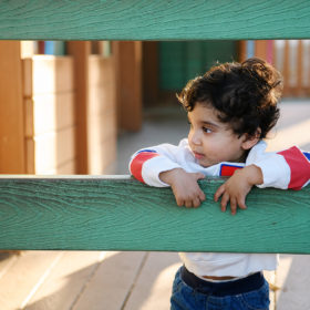 One year old boy leaning against green fence in McKinley Park playground