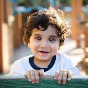 Baby boy smiling directly into camera on playground structure in McKinley Park Sacramento