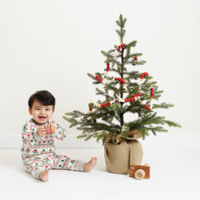 Baby boy wearing pajamas next to Christmas tree and toy camera