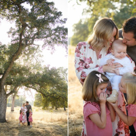 Family standing under large tree and kissing baby brother in Folsom