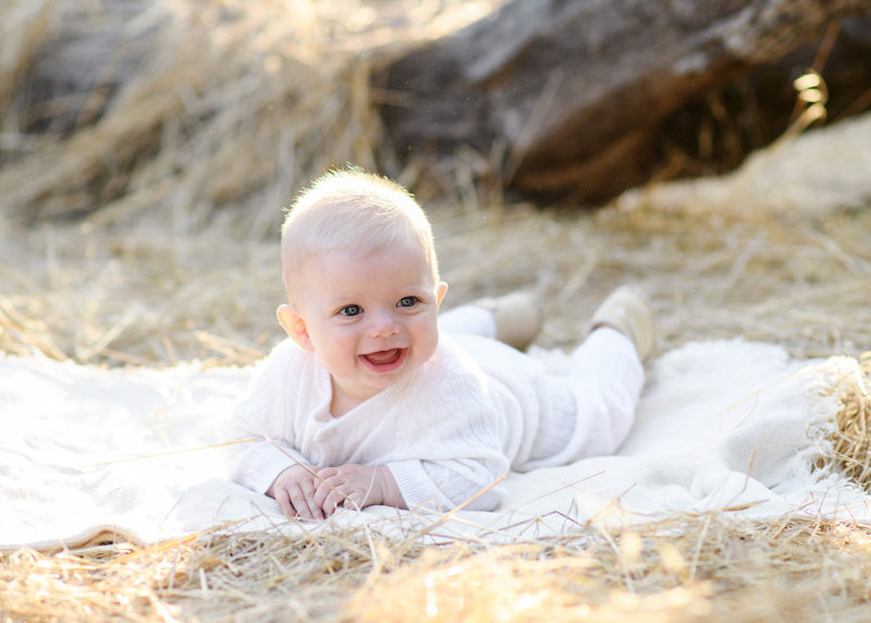 Baby boy wearing white lying on blanket on dry grass in Folsom