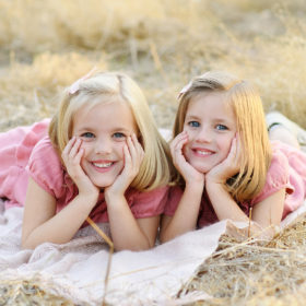 Twin sisters lying down on white blanket and smiling in Folsom