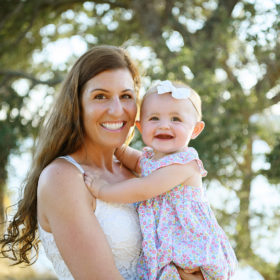 Mom holding baby daughter and smiling with trees in the background in Folsom