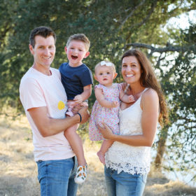 Family portrait with dad holding son and mom holding baby daughter outdoors by trees in Folsom