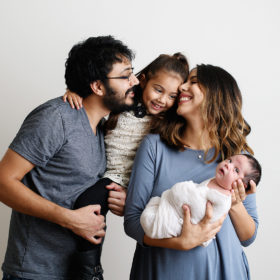 Family photo holding a newborn baby with big sister looking lovingly at baby in studio