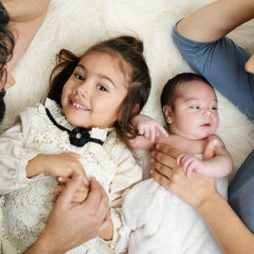 Aerial photo of family lying on sheepskin rug as big sister looks directly at camera next to newborn baby