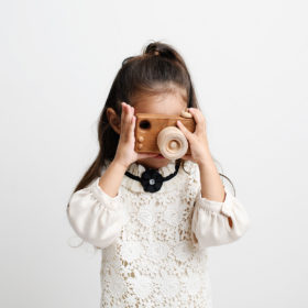 Big sister holding a wooden toy camera against white studio wall