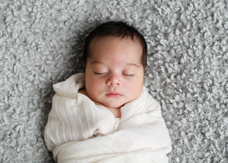 Sleeping newborn baby in muslin swaddle on gray blanket in studio