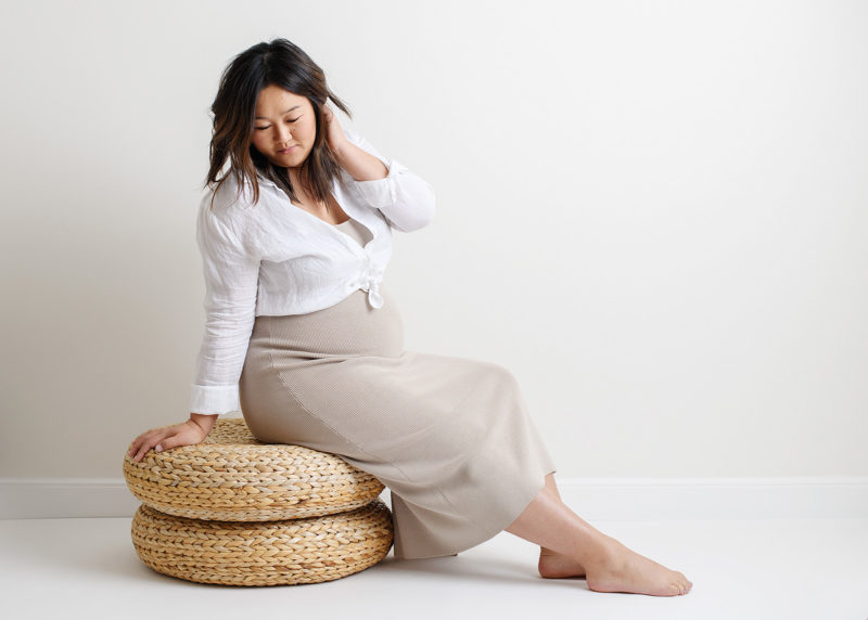 Maternity photo with pregnant Asian women sitting on rattan cushions in Sacramento studio