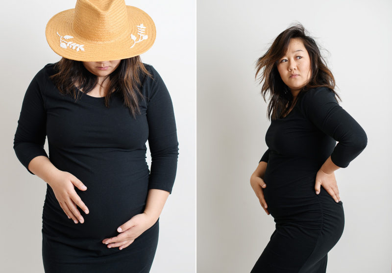 Maternity photo of pregnant Asian woman in black dress holding baby bump in Sacramento studio white wall