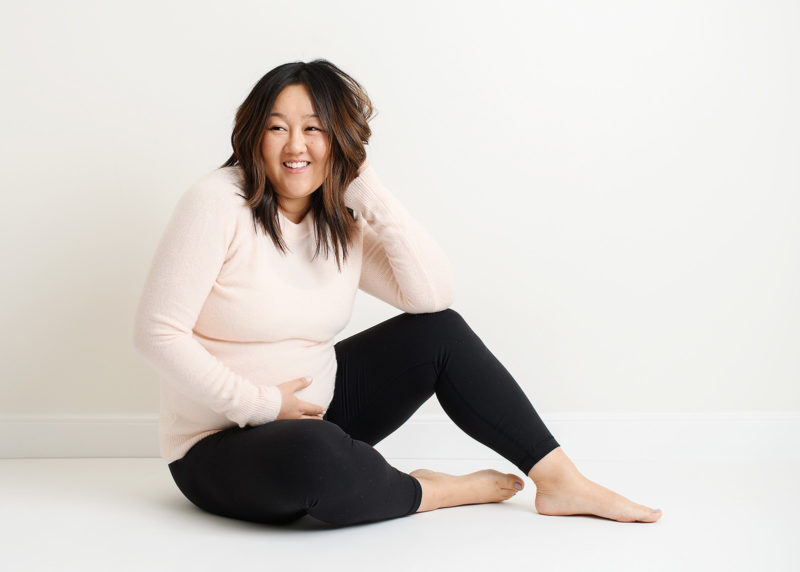 Maternity photo of pregnant Asian woman sitting on studio floor and smiling