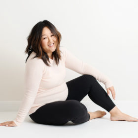 Pregnant Asian woman smiling and casually sitting on Sacramento studio floor