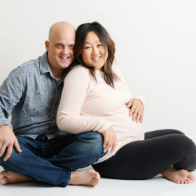 Pregnant mom and dad sitting on the floor and hugging in Sacramento studio