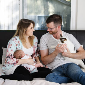 Mom holding newborn baby as dad holds on to cat in bed at home lifestyle photo
