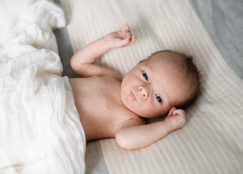 Newborn baby lying in bed at home while looking at camera lifestyle session