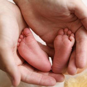 Tiny newborn baby feet being held by mom’s hands