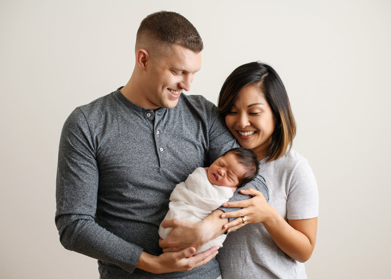 Mom and dad smiling at sleeping swaddled newborn baby girl in Sacramento studio