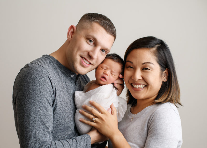 Dad and mom smiling as they hold their newborn baby daughter in Sacramento studio