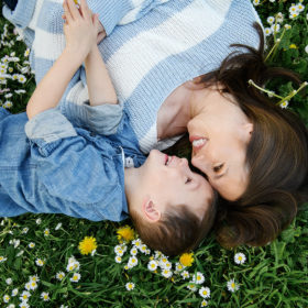 Mom and son lying on grass and smiling at each other aerial view next to wildflowers