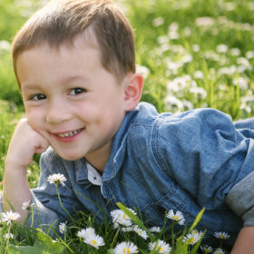 Little boy smiling with arm propping up his head and lying on grass and wildflowers in Land Park Sacramento