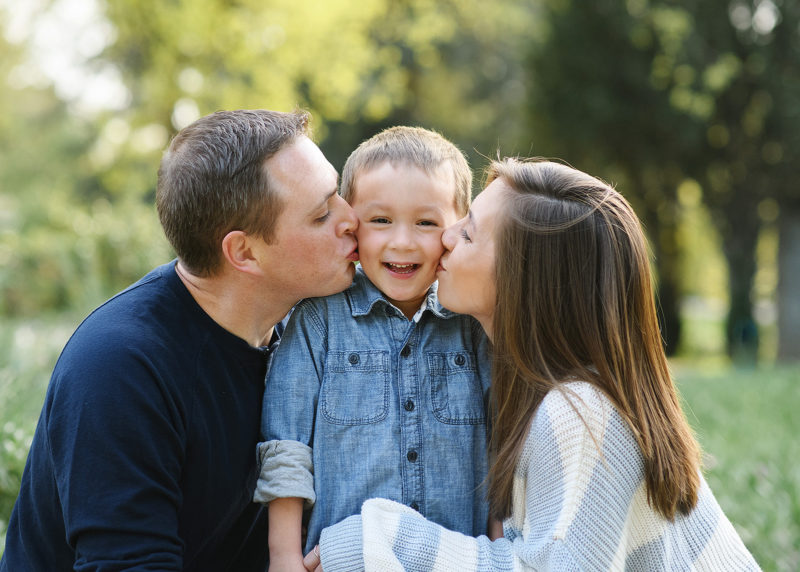 Dad and mom kissing son on cheek outdoors in Sacramento park