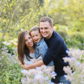 Mom and dad hugging son surrounded by flowers and greenery in Sacramento park