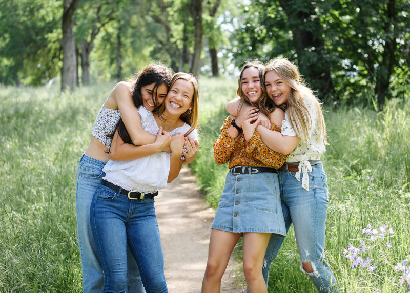 Friends hugging and smiling outdoors in park among green grass