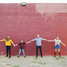 Family holding hands in front of red painted brick wall in midtown Sacramento