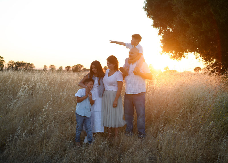 Family hugging each other on dry grass as sun sets in Sacramento