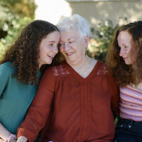 Grandma smiling and leaning into granddaughters in front of Sacramento home